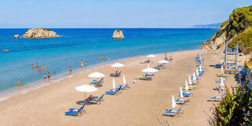 Organised sandy beach with turquoise waters, sunbeds, umbrellas and swimmers in southern Corfu