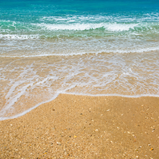 Gentle turquoise waves and white sea foam on a sandy beach in southern Corfu