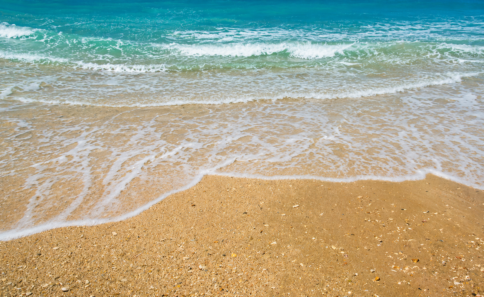 Gentle turquoise waves and white sea foam on a sandy beach in southern Corfu
