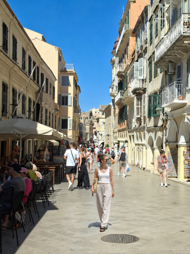 Sunny shopping street in Corfu Town with elegant buildings, cafés and a tourist walking through the Old Town